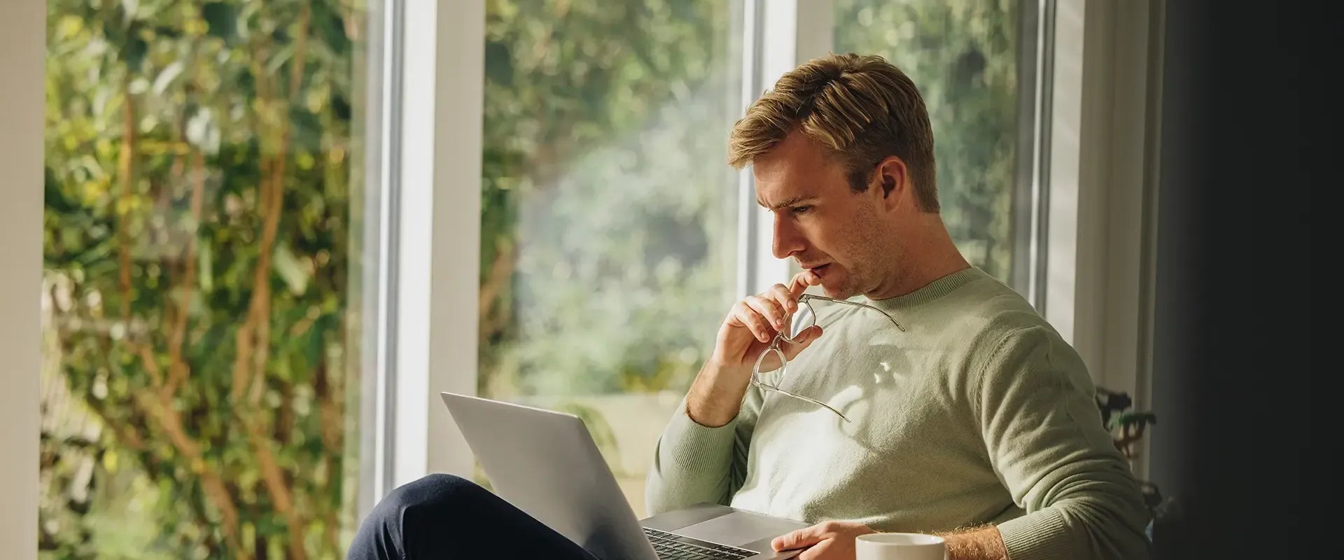 Man werkt geconcentreerd op een laptop bij een raam.
